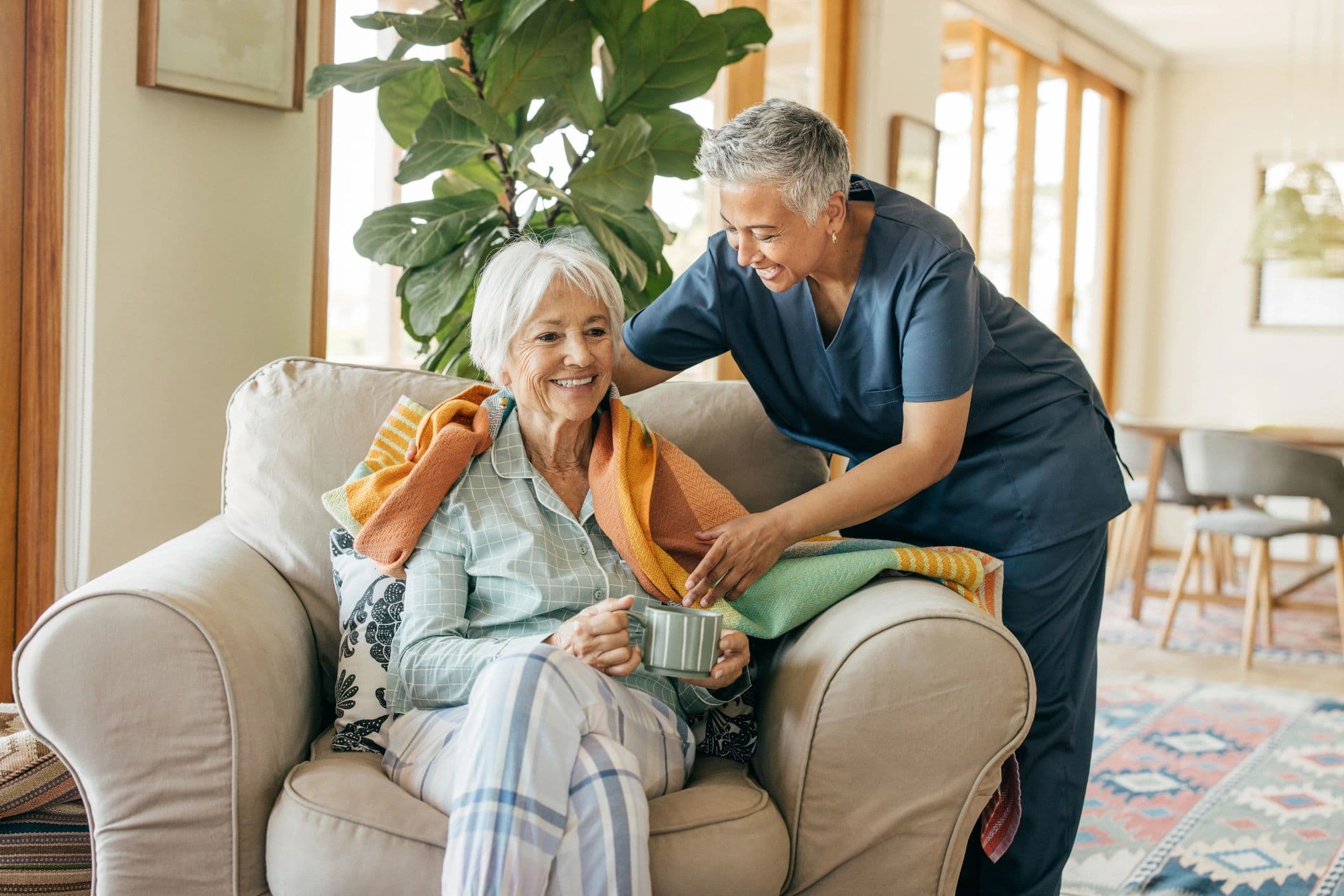 A caregiver tucking a blanket around an older woman